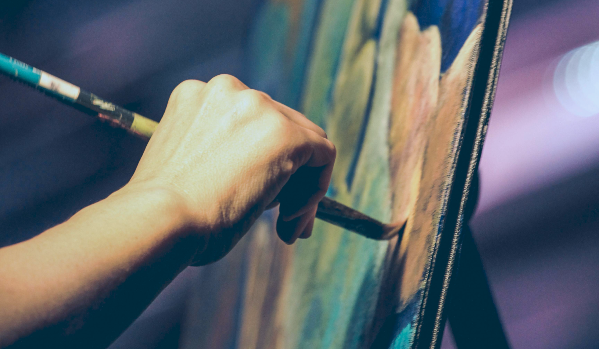 Hand holding paintbrush to green and brown canvas 